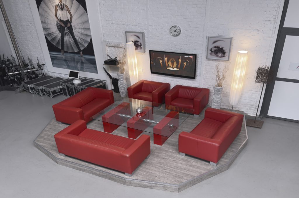 „Loungebereich im Studio von Arts Unlimited 4Rent mit roten Ledersofas, Glastisch und TV“